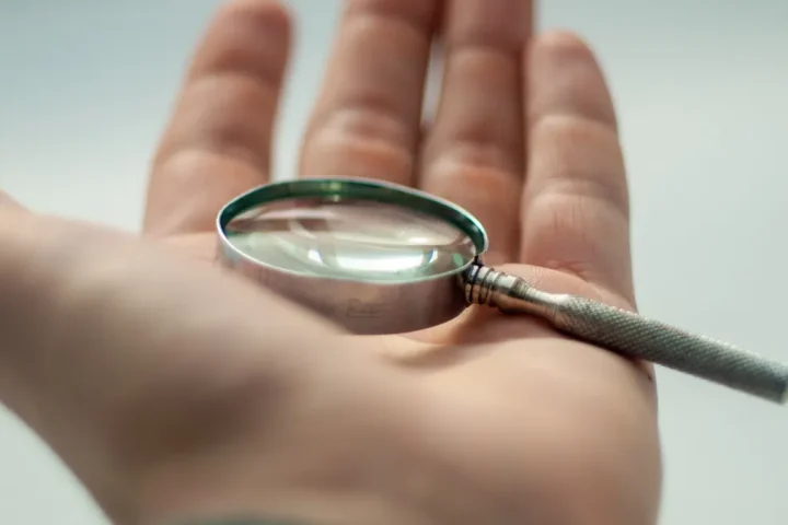 Magnifying glass in a hand, symbolizing scrutiny and verification