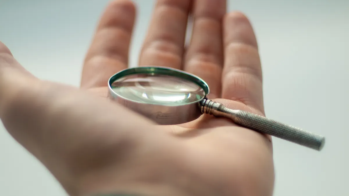 Magnifying glass in a hand, symbolizing scrutiny and verification