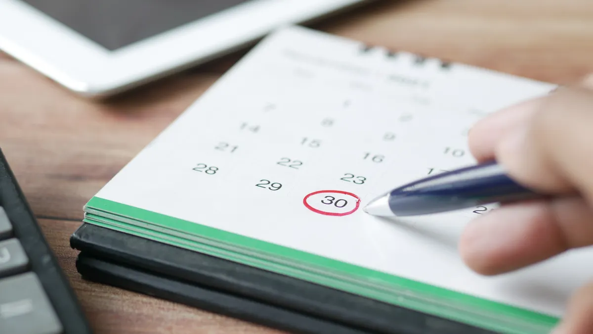 Hand writing on a paper calendar beside a laptop